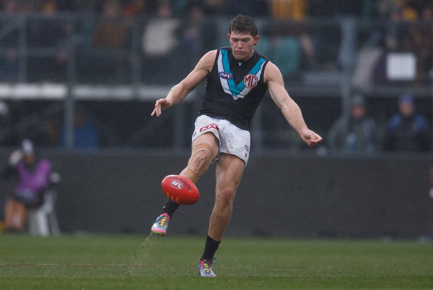 Port Adelaide AFL football player kicking a red ball during a match.