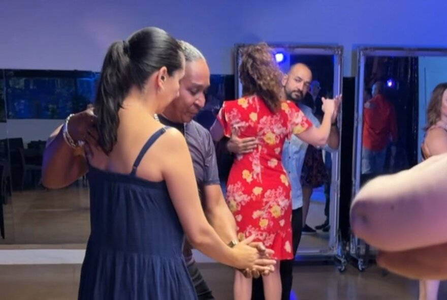 A couple salsa dancing together in a studio with other couples in the background.
