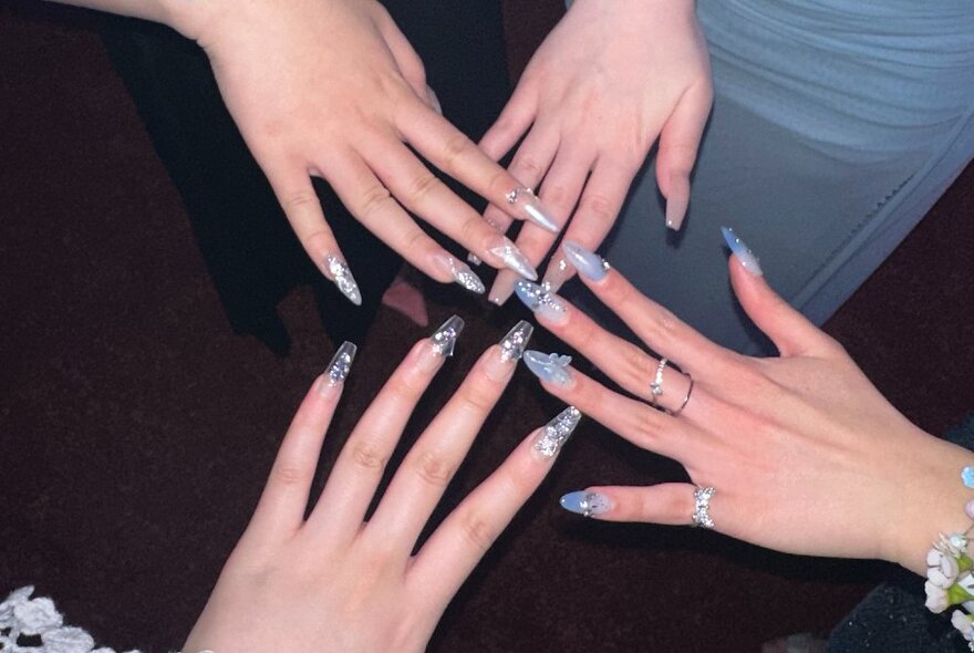 Hands wearing purple-toned long fake fingernails with sparkly decorations.