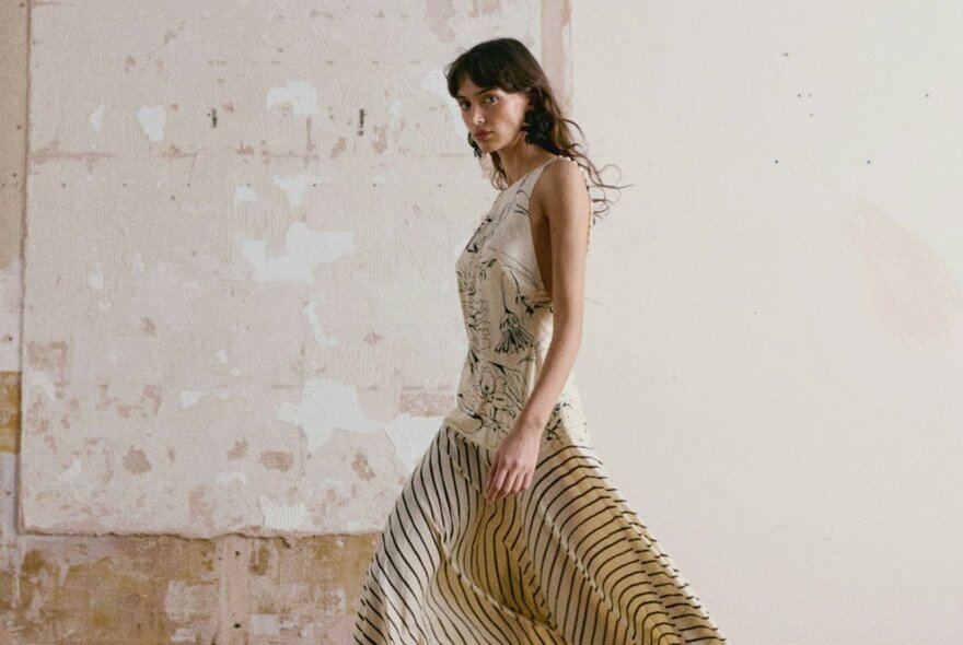 A model wearing a gauzy cream dress with black patterns on it.