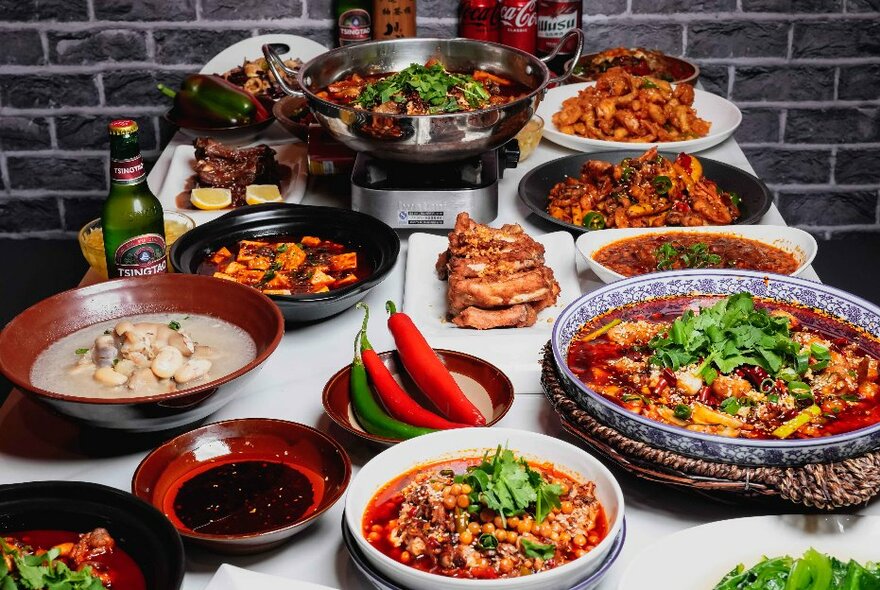 A banquet feast of many Chinese dishes and a big bowl of long chillies in the middle. 