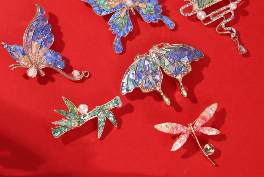 Decorative brooches that all use mother of pearl inlay, on a red background.