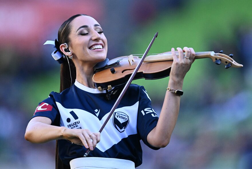 Woman wearing soccer jersey playing the violin.