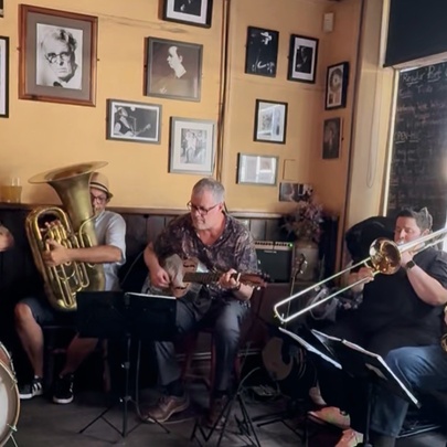 A band of five musicians seated inside the front bar of a pub all playing instruments.
