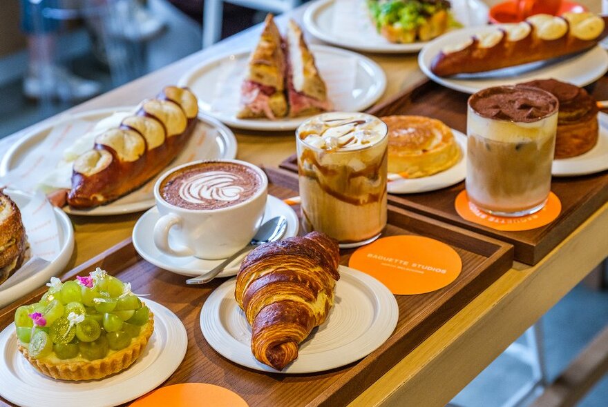 A table set with cafe dishes including coffees, pastries and pretzel baguettes.