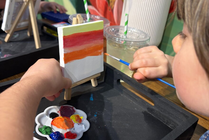 A child painting a mini easel with a brush and palette.