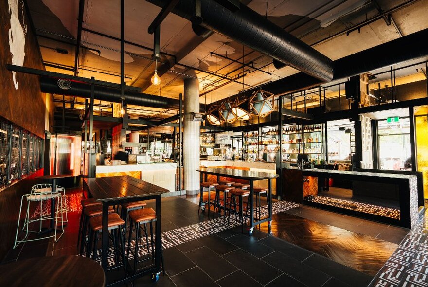 Inside of an industrial-look restaurant, with black bench tables and stools and exposed piping on the ceiling.