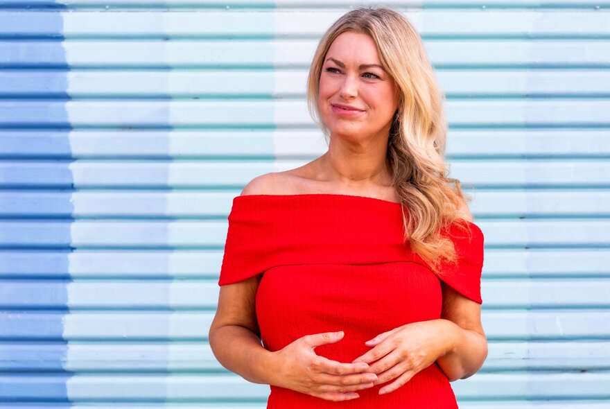 Woman in a red off-the-shoulder top with long blonde hair against a blue and white striped background. 