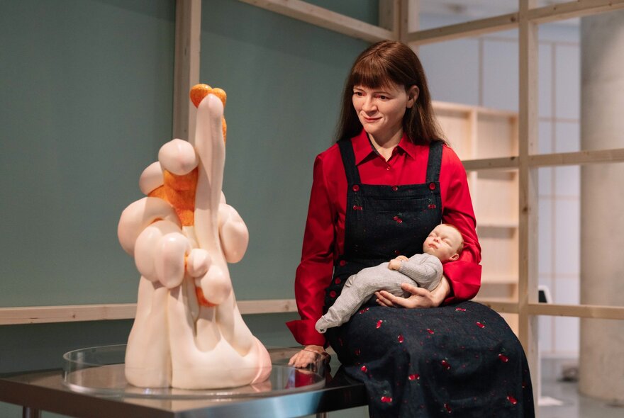 A sculpture of a young woman holding a baby, looking at a sculpture depicting a human-like form.