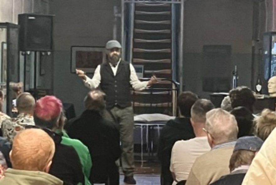 Author Roy Maloy wearing a cap and talking to a seated audience.