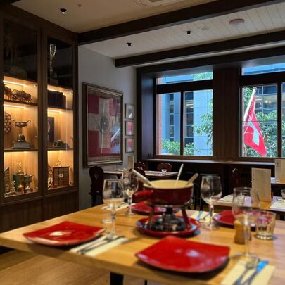 A table in small restaurant set with red plates and a fondue pot,  the Swiss flag visible through a window.