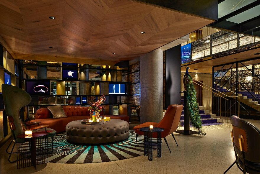 Moody hotel bar with dim lighting, wooden parquet ceiling and plush furnishings.