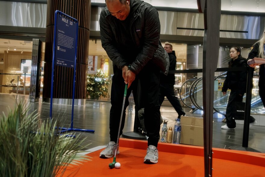 A person putting at a mini golf display in a shopping centre. 