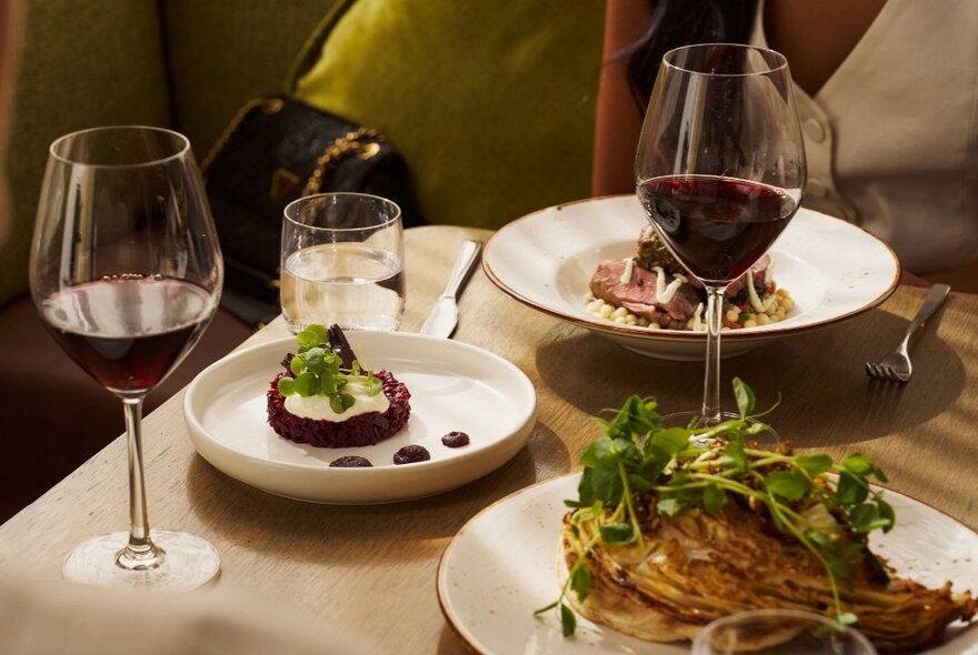 A table in a restaurant with two plates of food, and two glasses of red wine.