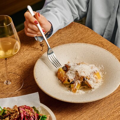 A woman eating pasta with a white wine.