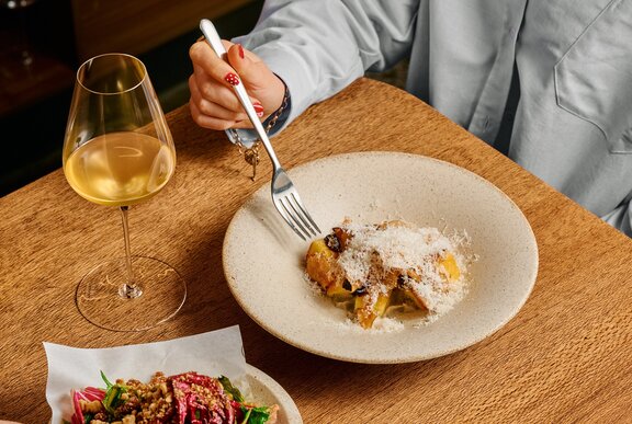 A woman eating pasta with a white wine.