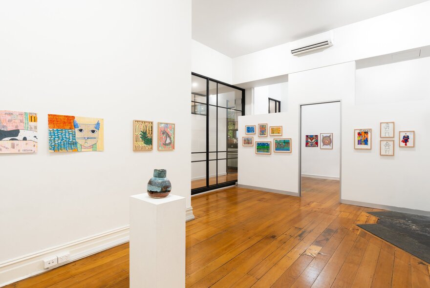 A gallery space with wooden floors and small colourful artworks lining the white walls.
