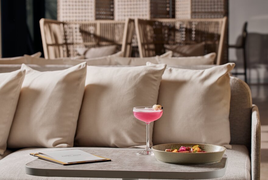 A beige couch in a modern restaurant with a pink cocktail on the marble table in front of it.