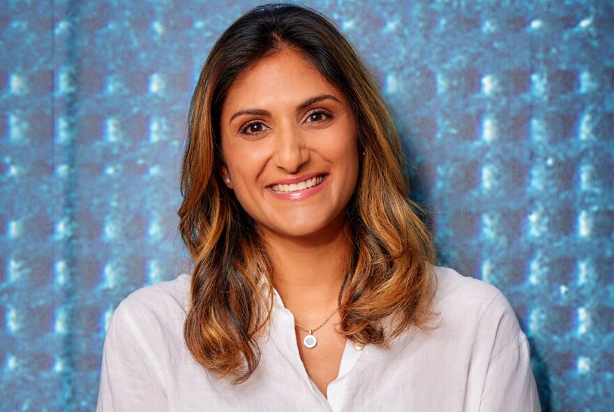 Dr Preeya Alexander, smiling openly against a blue waffle background. 