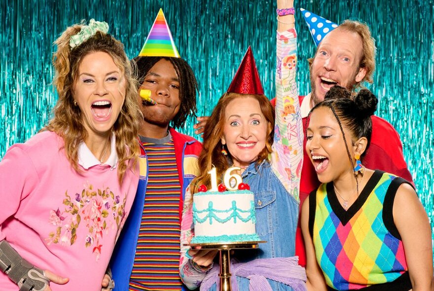 Five people wearing party hats holding a birthday cake with the numbers 16 in candles.