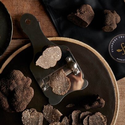 Looking down at a bowl of black truffles resting on a wooden board, with a truffle grater alongside.