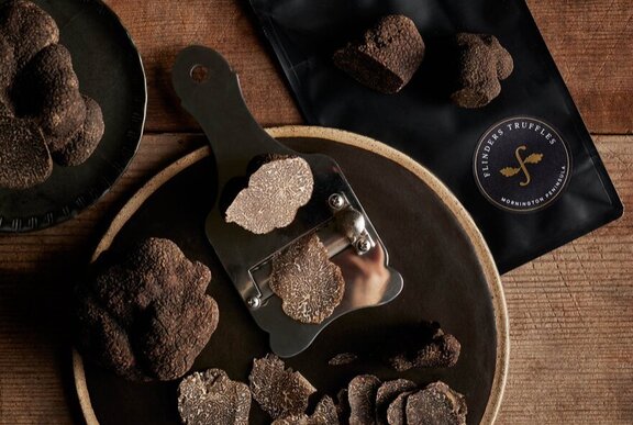 Looking down at a bowl of black truffles resting on a wooden board, with a truffle grater alongside.
