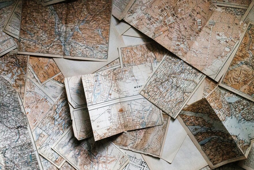 Looking down from above at paper cartographic maps, some folded and creased, other open and spread out.