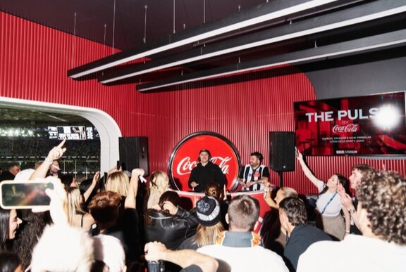 A DJ spinning tracks at a black and red venue, with patrons dancing in front of him.