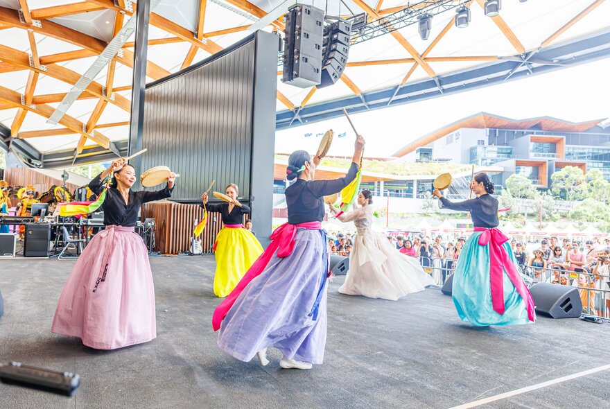 Dancers in long traditional gowns performing on a stage with ribbons and tambourines.