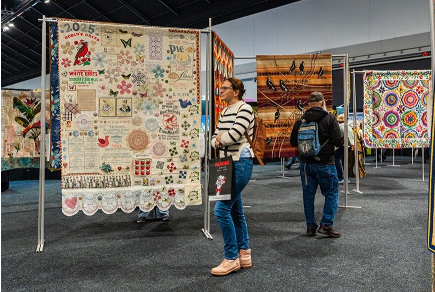 Visitors admiring large handmade textile art and quilts at a craft and quilting exhibition.