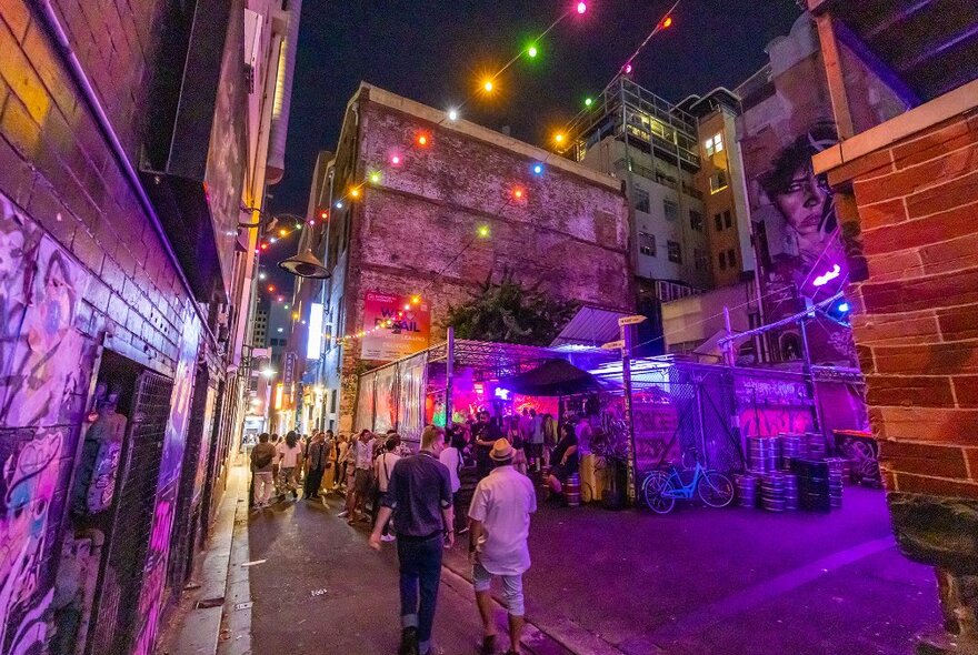 People walking towards a laneway bar with colourful lights at night.