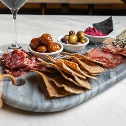 A table with a glass of wine and charcuterie board with olives, small goods and cheese 
