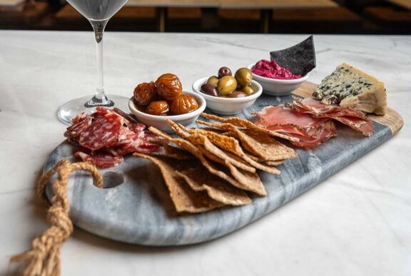 A table with a glass of wine and charcuterie board with olives, small goods and cheese 