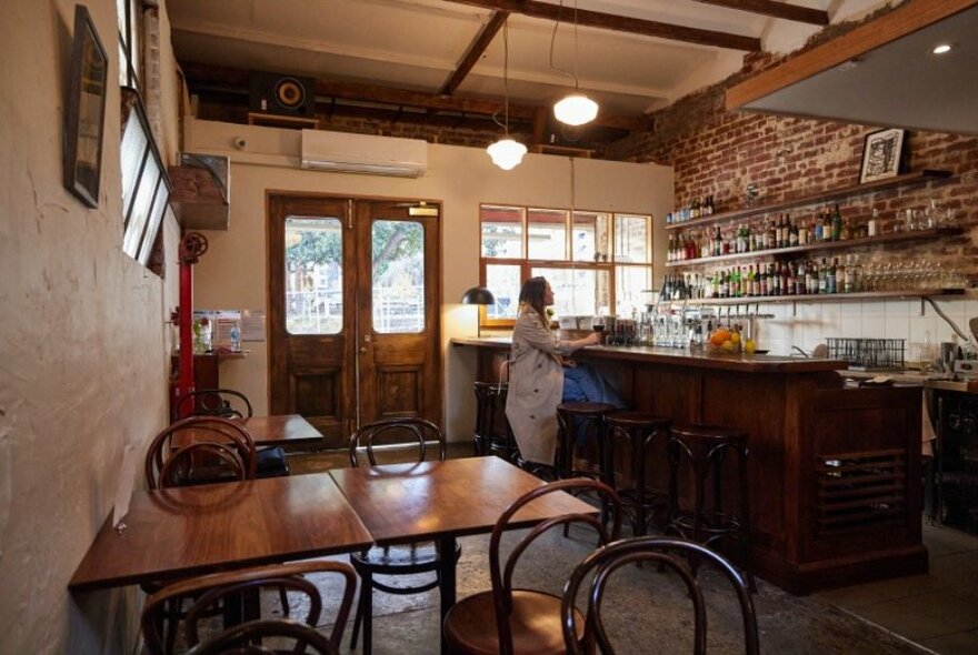 Interior of Bar Holiday, cafe with bar facing brick wall on right hand side, wooden tables on left.