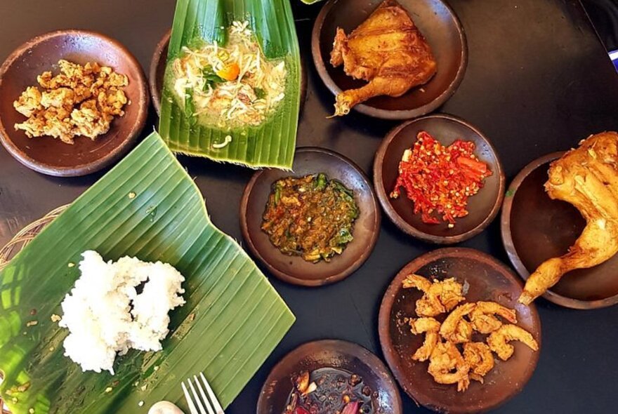 Indonesian dishes on a table, including sambal sauces, rice on pandanus leaf, prawns and chicken.