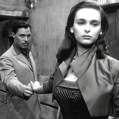 A still from the black and white film The Lady without Camelias showing a woman walking away from a man while still holding his hand. 