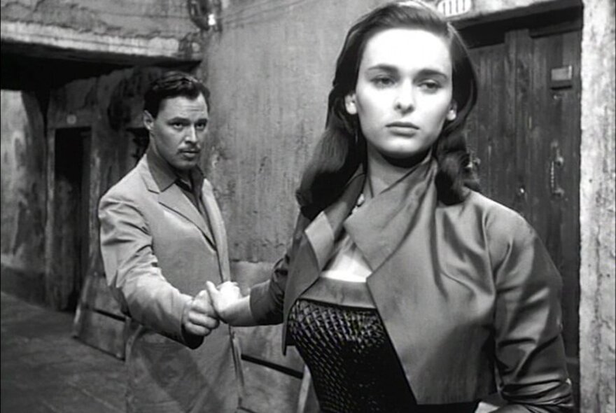 A still from the black and white film The Lady without Camelias showing a woman walking away from a man while still holding his hand. 