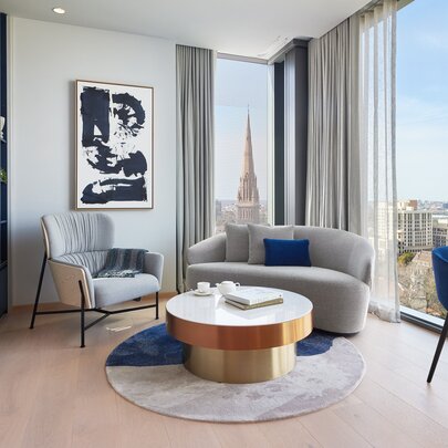 A stylish lounge room area in a hotel room with floor to ceiling windows looking out over Melbourne.
