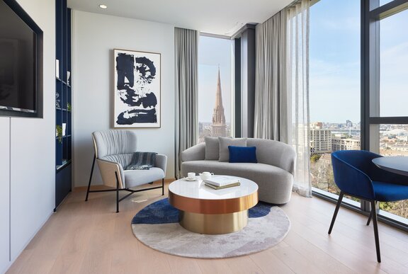 A stylish lounge room area in a hotel room with floor to ceiling windows looking out over Melbourne.