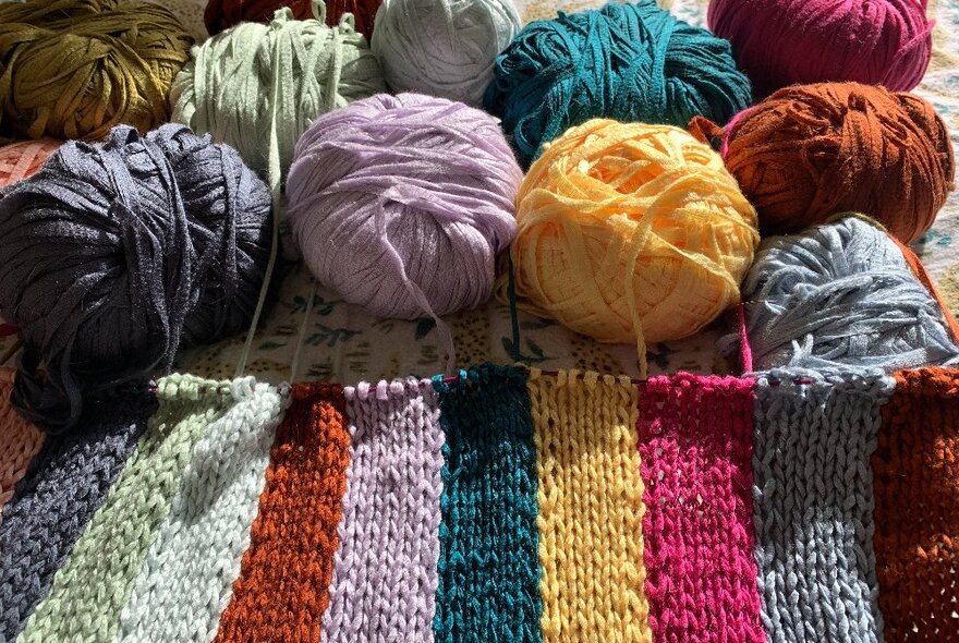 Balls of coloured yarn arranged in front of a portion of knitting in similar colours.