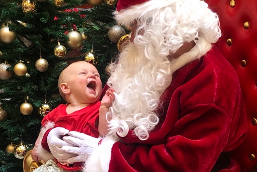 Santa holding a giggling baby in front of a Christmas tree.