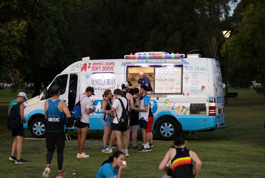 People relaxing in a park, wearing running gear, with a food truck in the background.