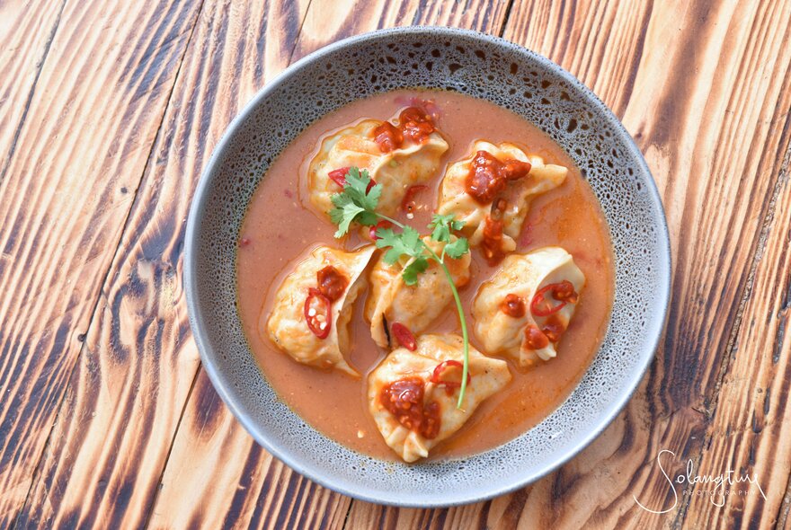A bowl of dumplings in a coconut broth with chilli garnish. 
