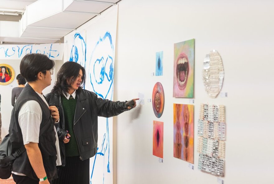 Two people standing in a gallery looking at contemporary artworks on the white walls.