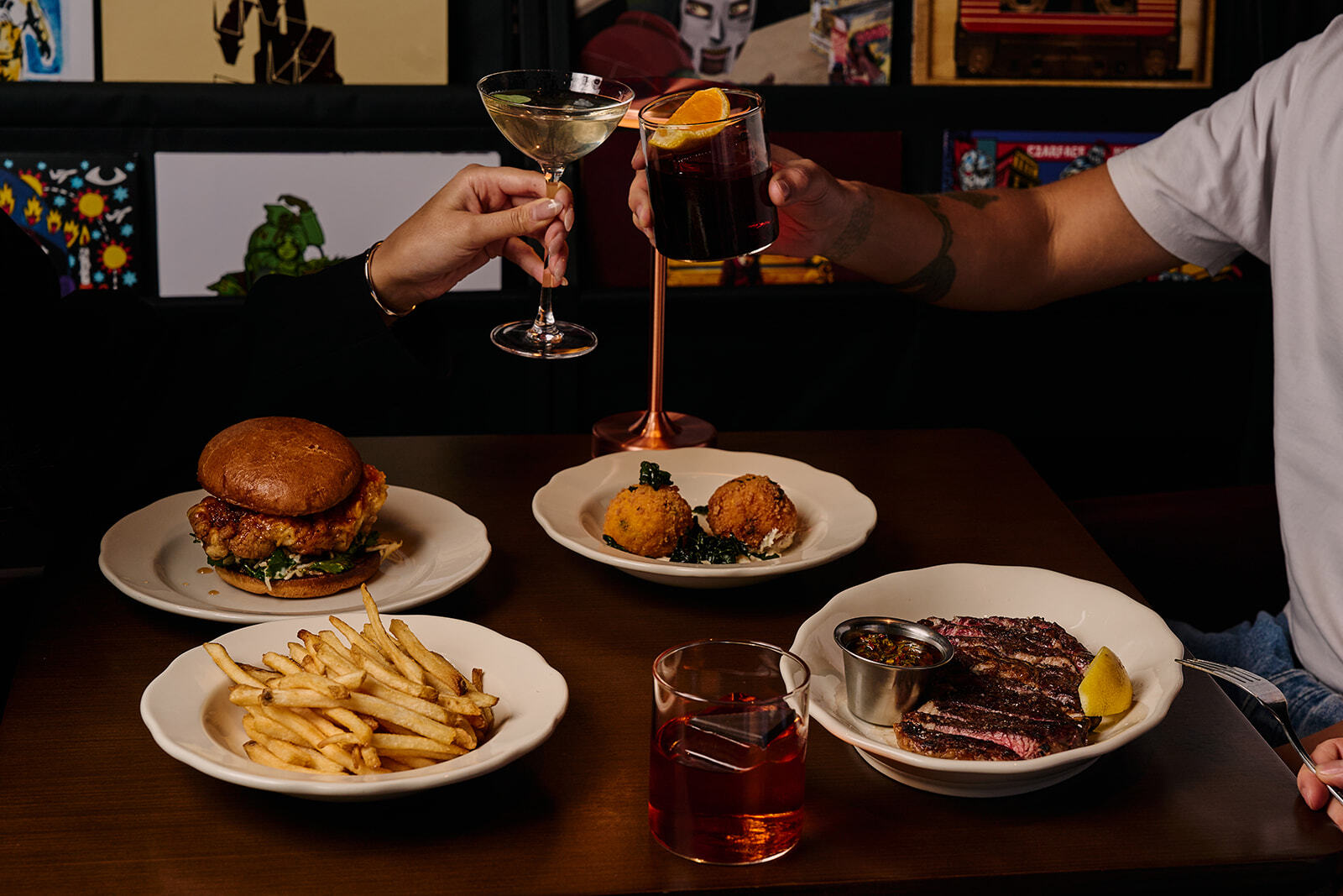 A table filled with steak, burger and chips while cocktails are raised above.