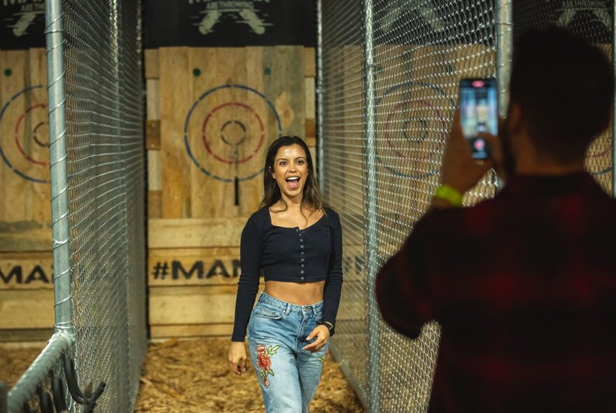 A happy woman walking along a narrow caged area after throwing a bullseye at an axe-throwing venue.
