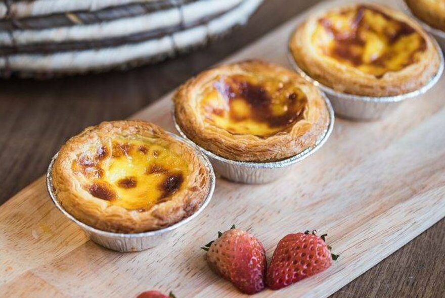 Three egg tarts on a wooden board.