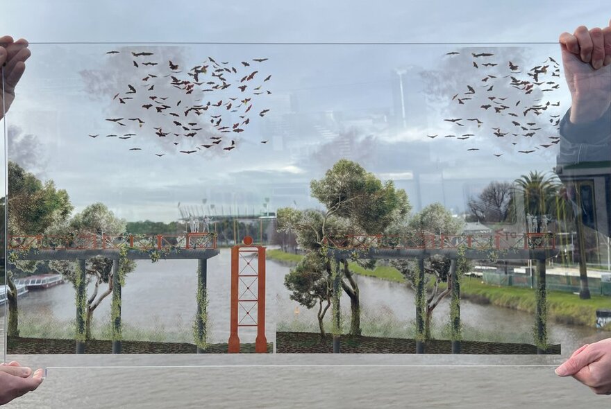 Two sets of hands holding up a pane of clear glass painted with trees and birds, behind it a river and river banks.