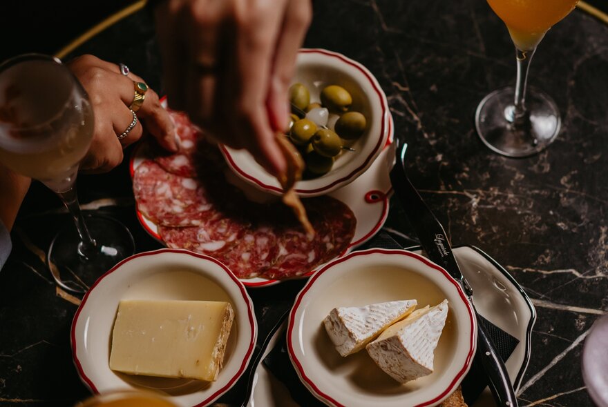 Looking down on a table with small plates of sliced salami, cheese and olives. 
