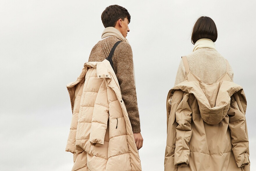 Two people with coats hanging off straps on their backs.